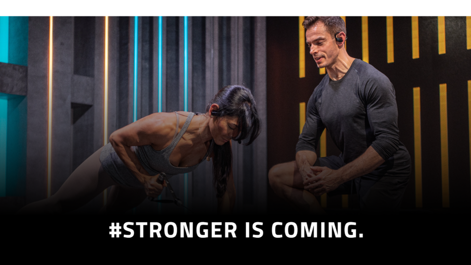 35 - Two athletes training in a neon-lit gym; woman performs a push-up with a band while a man watches, caption '#STRONGER IS COMING.'